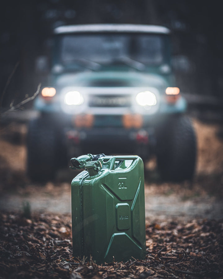 Olive drab Wavian 20L jerry can in front of a Toyota FJ40 with headlights on