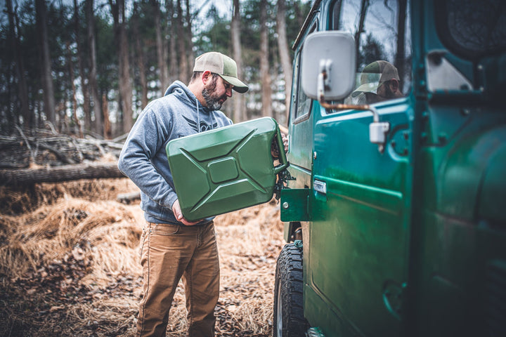Man loading an olive drab Wavian 20L jerry can onto the side mount of a Toyota FJ40