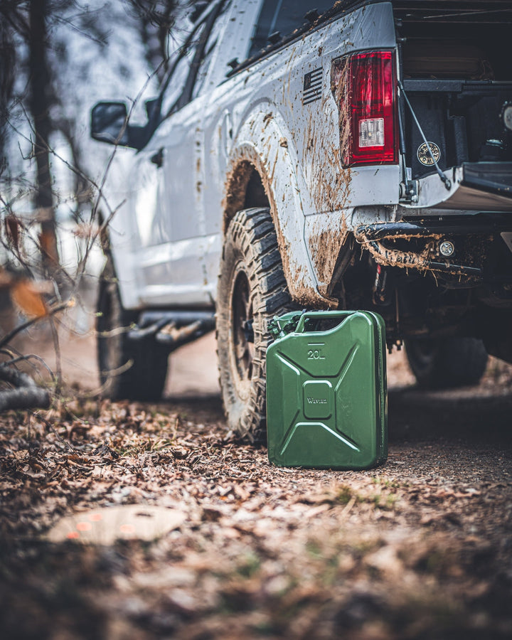 Olive drab Wavian 20L jerry can beside a mud-covered pickup truck